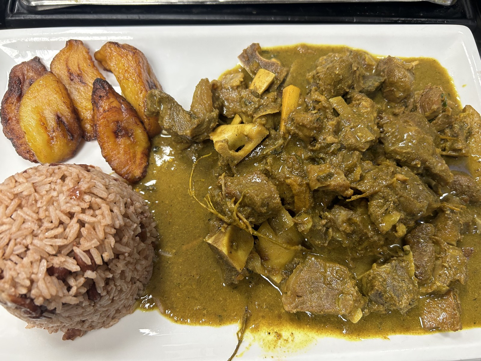 Curry goat with rice and peas and fried plantains